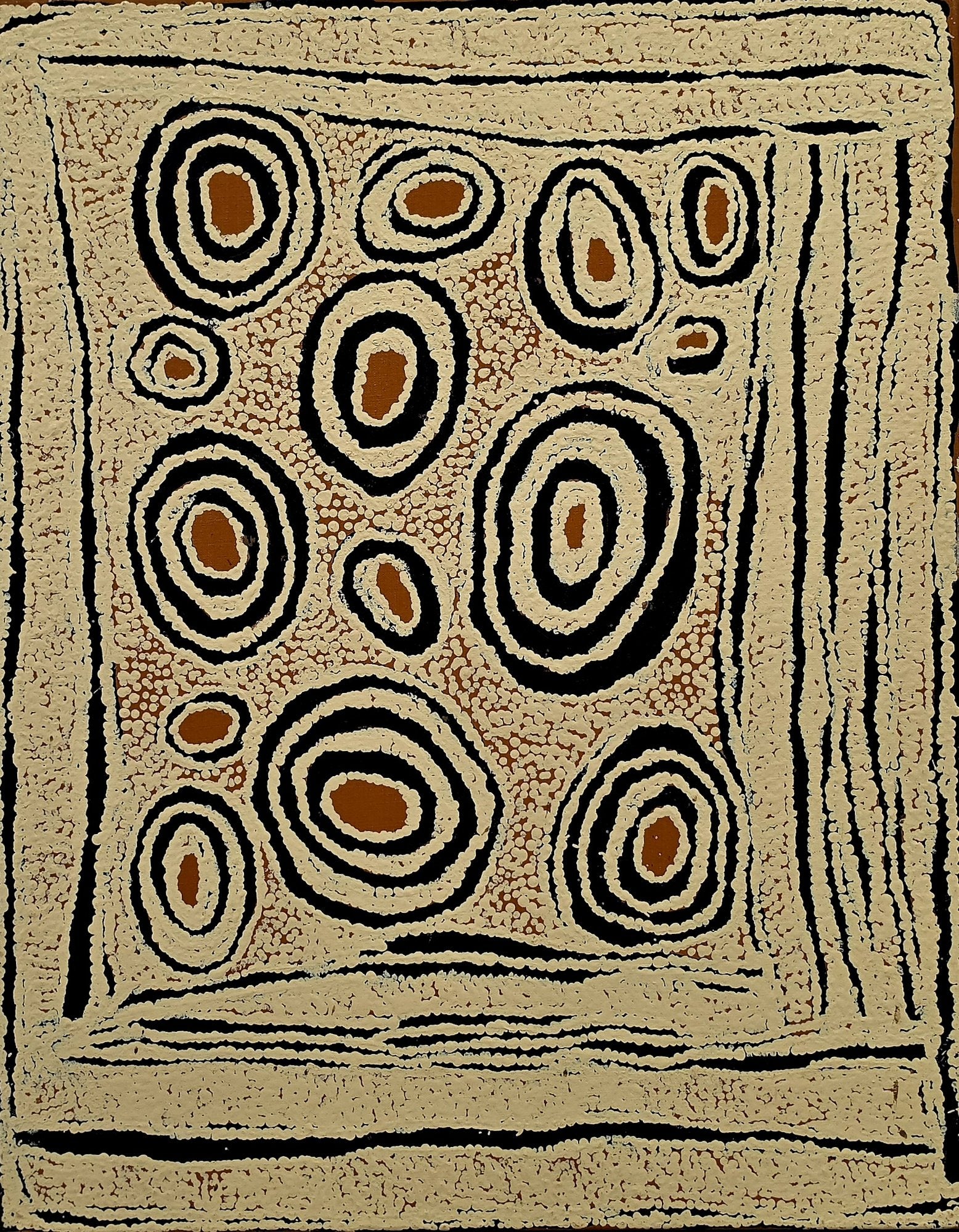 Western Desert painting with clusters of concentric ovals in ochre, cream and black on a densely dotted sandy ground, bordered by vertical striations.