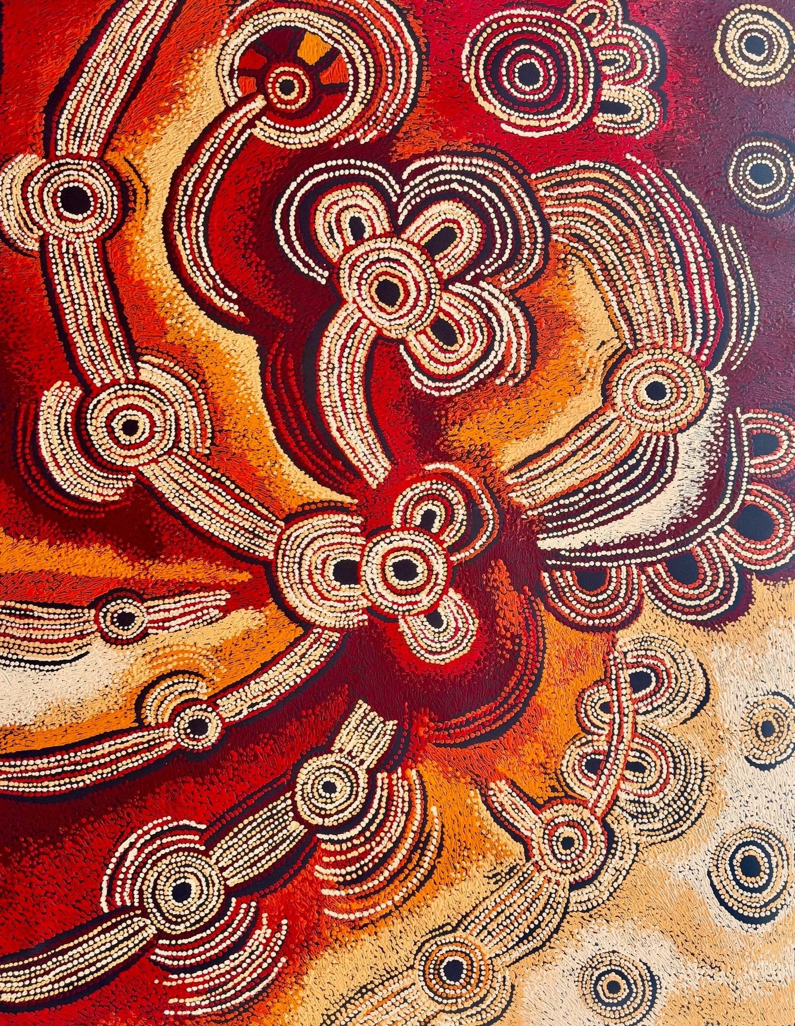 Large dot painting in deep red, orange and cream featuring clustered concentric circles linked by long ribbed curving lines, evoking desert sites connected across country.